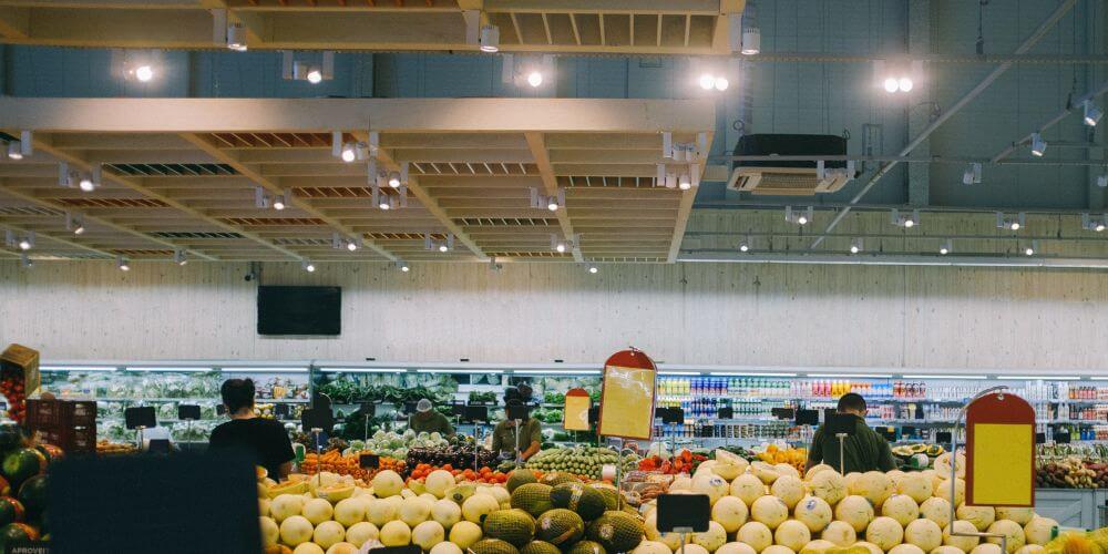 Área de frutas e legumes em supermercado iluminada por projetores de calha